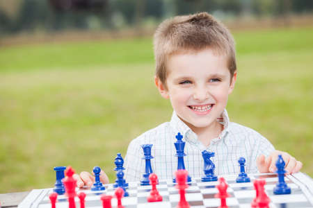 Elegant young boy in white shirt learning to play chess with blue and red chess pieces on wood table in the parkの写真素材