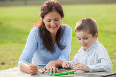 Young woman teacher teaches little young boy in white shirt painting with the brush to make artisanal pasta beadsの写真素材
