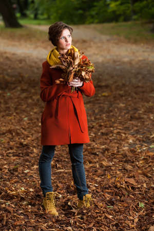 Beauty romantic girl holding a bunch of rusty leaves in autumn dayの写真素材