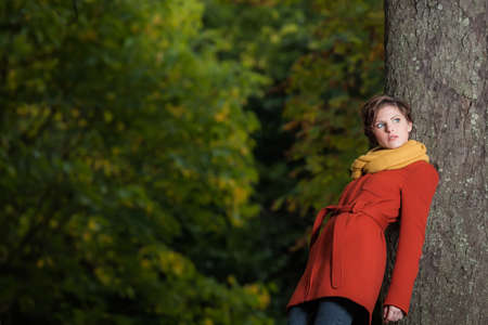 Sexy beautiful serious romantic girl with short hair leaning against a treeの写真素材
