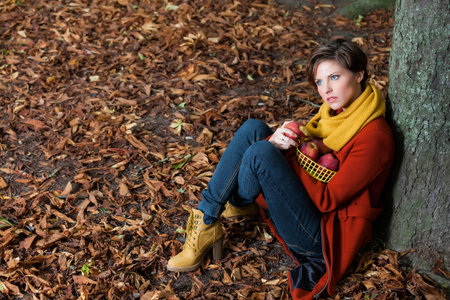 Sexy beautiful serious romantic girl sitting against a tree eating an apple in the park