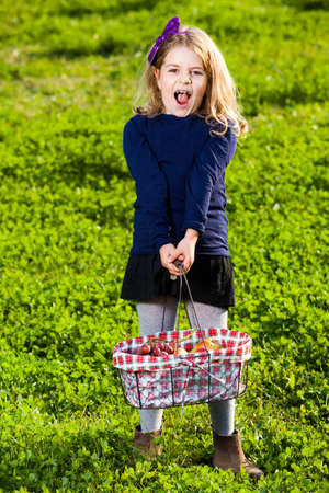 happy girl child holding picnic basket with fruits on the green grassの写真素材
