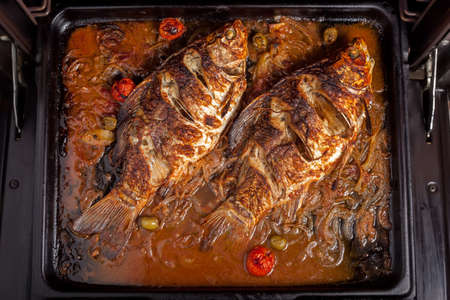 Two carp fishes prepared to be cooked in the oven with tomatoes, olives onion pepper, bay leaf and  tomato sauceの写真素材