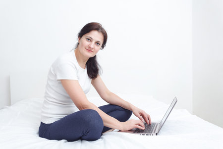 similg happy woman sit in bed with a laptop working from homeの写真素材