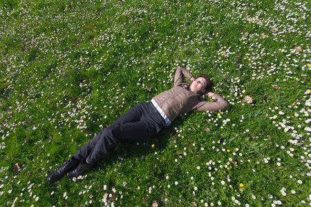 Relaxing young woman in pants and leather jacket lying on grass and spring flowersの写真素材