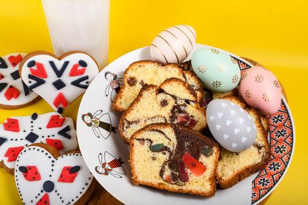 Slices of Romanian sponge cake with red traditional towel with manual stitch on wooden board, Easter painted eggs and home made ginger bread hearts, Authentic Easter Brunch concept.の写真素材