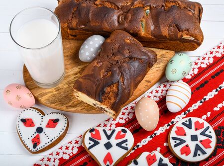Slices of Romanian sponge cake with red traditional towel with manual stitch on wooden board, Easter painted eggs and home made ginger bread hearts, Authentic Easter Brunch concept.の写真素材