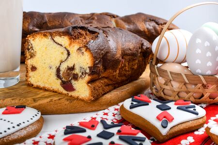 Slices of Romanian sponge cake with red traditional towel with manual stitch on wooden board, Easter painted eggs and home made ginger bread hearts, Authentic Easter Brunch concept.の写真素材