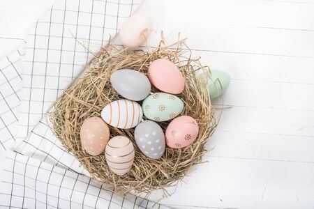 Easter table setting, holiday table home decor idea, flat lay composition with white plates, cutlery, colorful pastel painted Easter eggs, festive decor and fresh spring flowersの写真素材
