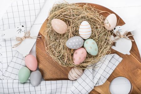 Easter table setting, holiday table home decor idea, flat lay composition with white plates, cutlery, colorful pastel painted Easter eggs, festive decor and fresh spring flowersの写真素材
