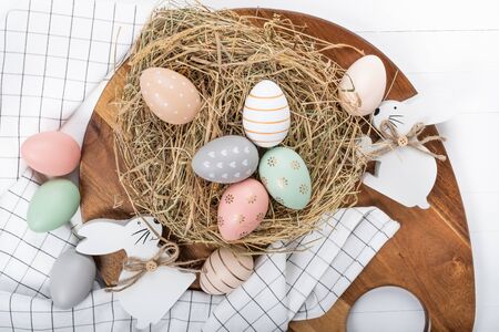 Easter table setting, holiday table home decor idea, flat lay composition with white plates, cutlery, colorful pastel painted Easter eggs, festive decor and fresh spring flowersの写真素材