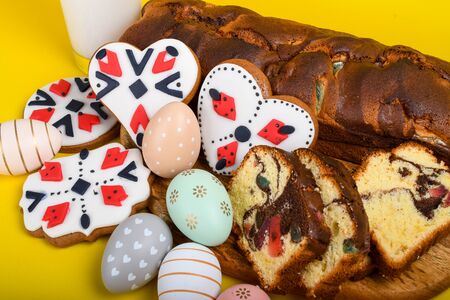 Slices of Romanian sponge cake with red traditional towel with manual stitch on wooden board, Easter painted eggs and home made ginger bread hearts, Authentic Easter Brunch concept.の写真素材