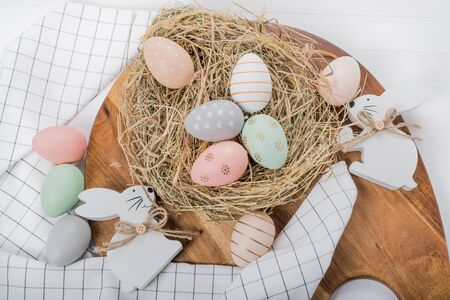 Easter table setting, holiday table home decor idea, flat lay composition with white plates, cutlery, colorful pastel painted Easter eggs, festive decor and fresh spring flowersの写真素材
