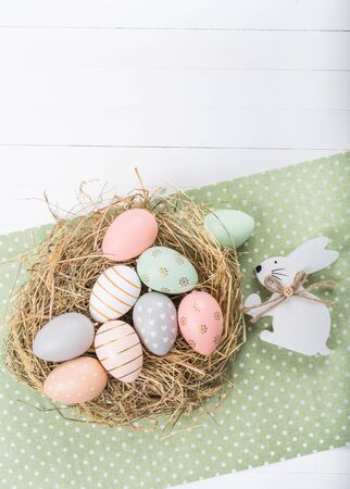 Easter table setting, holiday table home decor idea, flat lay composition with white plates, cutlery, colorful pastel painted Easter eggs, festive decor and fresh spring flowersの写真素材