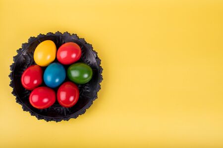 Wicker basket of colorful Easter eggs isolated on yellow, simple clean concept, with copy space for text visualの写真素材