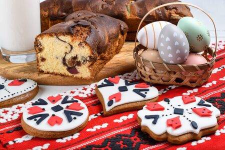 Slices of Romanian sponge cake with red traditional towel with manual stitch on wooden board, Easter painted eggs and home made ginger bread hearts, Authentic Easter Brunch concept.の写真素材