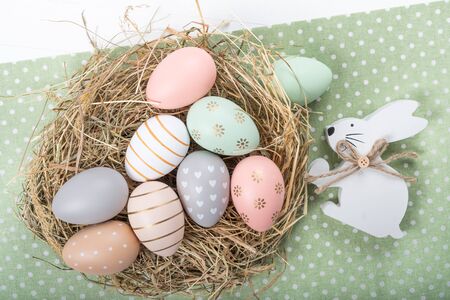 Easter table setting, holiday table home decor idea, flat lay composition with white plates, cutlery, colorful pastel painted Easter eggs, festive decor and fresh spring flowersの写真素材
