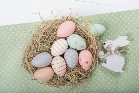 Easter table setting, holiday table home decor idea, flat lay composition with white plates, cutlery, colorful pastel painted Easter eggs, festive decor and fresh spring flowersの写真素材