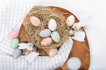 Easter table setting, holiday table home decor idea, flat lay composition with white plates, cutlery, colorful pastel painted Easter eggs, festive decor and fresh spring flowersの写真素材