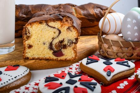 Slices of Romanian sponge cake with red traditional towel with manual stitch on wooden board, Easter painted eggs and home made ginger bread hearts, Authentic Easter Brunch concept.の写真素材
