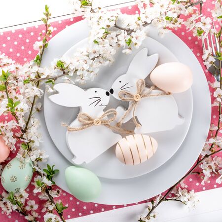 Easter table setting, holiday table home decor idea, flat lay composition with white plates, cutlery, colorful pastel painted Easter eggs, festive decor and fresh spring flowersの写真素材