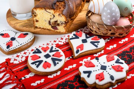 Slices of Romanian sponge cake with red traditional towel with manual stitch on wooden board, Easter painted eggs and home made ginger bread hearts, Authentic Easter Brunch concept.の写真素材