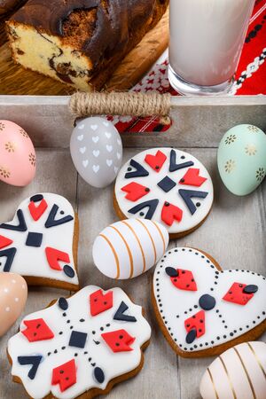 Slices of Romanian sponge cake with red traditional towel with manual stitch on wooden board, Easter painted eggs and home made ginger bread hearts, Authentic Easter Brunch concept.の写真素材