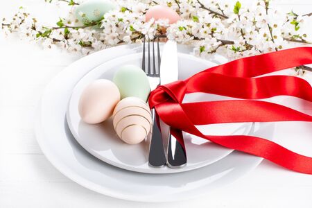 Easter table setting, holiday table home decor idea, flat lay composition with white plates, cutlery, colorful pastel painted Easter eggs, festive decor and fresh spring flowersの写真素材