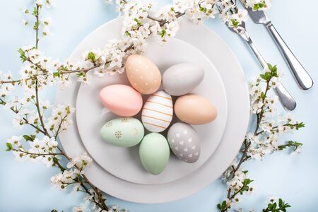 Easter table setting, holiday table home decor idea, flat lay composition with white plates, cutlery, colorful pastel painted Easter eggs, festive decor and fresh spring flowersの写真素材