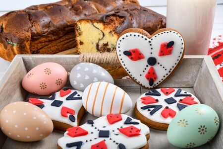 Slices of Romanian sponge cake with red traditional towel with manual stitch on wooden board, Easter painted eggs and home made ginger bread hearts, Authentic Easter Brunch concept.の写真素材