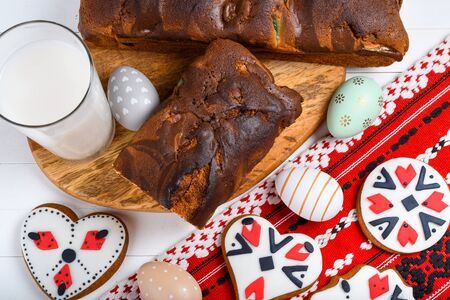 Slices of Romanian sponge cake with red traditional towel with manual stitch on wooden board, Easter painted eggs and home made ginger bread hearts, Authentic Easter Brunch concept.の写真素材
