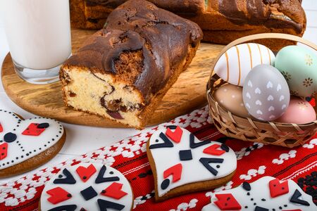 Slices of Romanian sponge cake with red traditional towel with manual stitch on wooden board, Easter painted eggs and home made ginger bread hearts, Authentic Easter Brunch concept.の写真素材