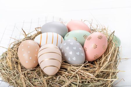Easter table setting, holiday table home decor idea, flat lay composition with white plates, cutlery, colorful pastel painted Easter eggs, festive decor and fresh spring flowersの写真素材