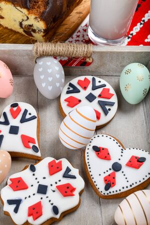 Slices of Romanian sponge cake with red traditional towel with manual stitch on wooden board, Easter painted eggs and home made ginger bread hearts, Authentic Easter Brunch concept.の写真素材