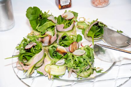Fresh dark leafy greens salad lettuce mix with cucumbers, arugula, radishes dressing on a plate during breakfast buffet or brunch catering event, food pliers on the plate. Vegetarian and vegan dishの写真素材