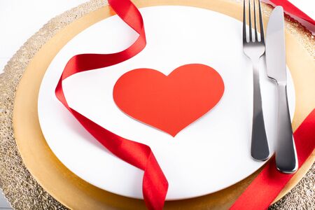 Romantic festive dinner with white empty plate with cutlery fork and knife over and red satin ribbon, with copy space, heart shapeの写真素材
