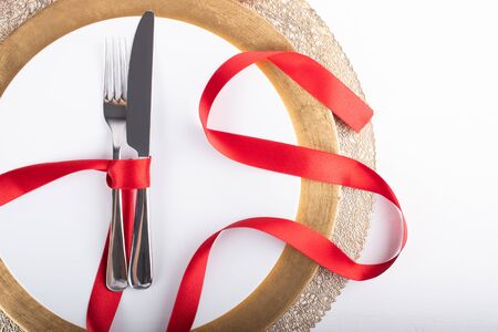Romantic festive dinner with white empty plate with cutlery fork and knife over and red satin ribbon, with copy space, heart shapeの写真素材