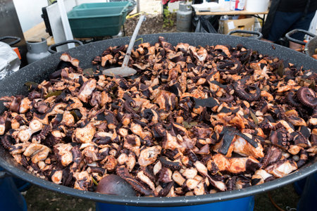 Boiled and seasoned with spices chopped pieces of octopus bites, cooking in a large wok, during food...