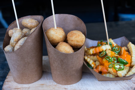 Group of Sicilian arancini in a brown paper cones and French fried potatoes with cheese cream and...