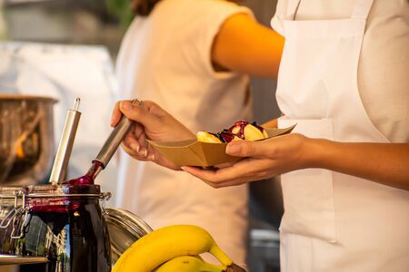 Woman pouring sweet fruit jam over doughnuts during fast food festival. Food truck. Outside catering. Food Buffet Catering Dining Eating Party Sharing Concept.の写真素材