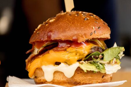 Fresh melting burger ready to eat during fast food festival. Outdoor catering event, brunch or outside dinner party with fast food. Melting cheese and golden bun. Appetizing closeup homemade burgerの写真素材