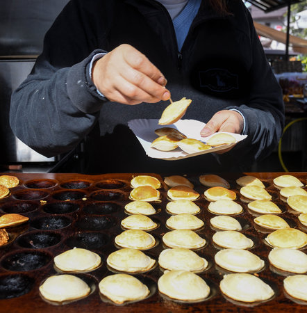 Typical Dutch poffertjes - tiny pancakes-being baked on a heavy cast iron pan being prepared during street food festival, an outdoor event, traditional dessert served with chocolate sauce and sugarの写真素材