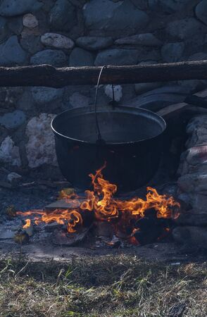 Very large cauldron cooking food during campfire, big pots on fire preparing during food festival. Tourist pot hanging over the fire . Cooking in a pot on the fire. Camping conceptの写真素材