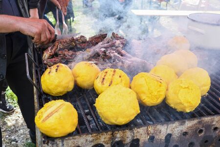 Balls of polenta and cheese in the middle of it, named bulz, a traditional romanian dish. Roasting polenta and cheese on a grill outside, with sheep sheep herdingの写真素材
