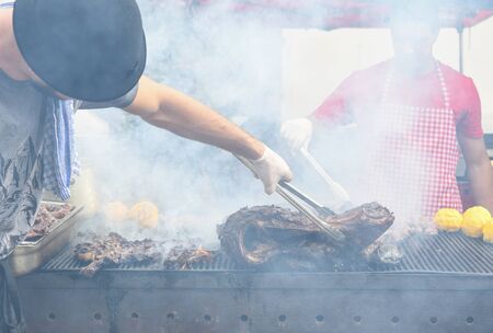 Chef hands cooking a very large piece of meat on the grill. Chef grilling meat on outside outdoor barbecue concept during summer food festival. BBQ event cooking and preparing food for guests. Assorteの写真素材