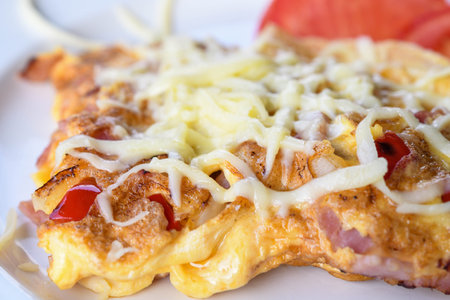 Traditional peasant omelette with ham, cheese, tomatoes, red peppers, bacon isolated and served on a...