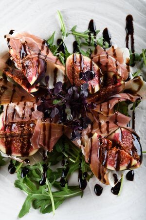 Traditional Italian salad made with figs, Prosciutto dry-cured ham or Parma ham thinly sliced prosciutto crudo served on a white plate in an Italian Restaurantの写真素材