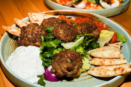 Mediterranean meatballs with salad, chickpeas with tomato sauce, yogurt dip and pita bread served in a restaurant setting background wooden table.の写真素材