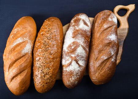Many mixed breads and rolls shot from above. Top view of assortment of different kind of cereal bakery: bread, pasties, buns, pretzel and croissant on old wooden background.の写真素材