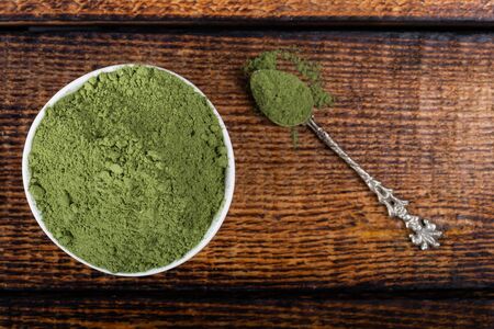 An isolated tablespoon of dried organic wheat grass and spirulina powder, on white or rustic background. Healthy living, detox recipes, raw vegan smoothie or juice ingredientsの写真素材